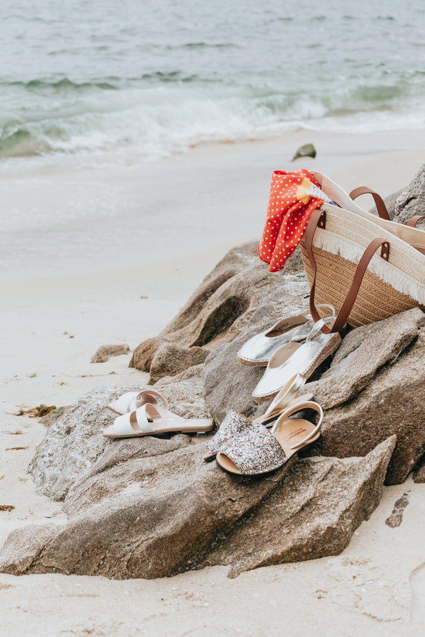 Three pairs of sandals and a beach bag on rocks by the beach
